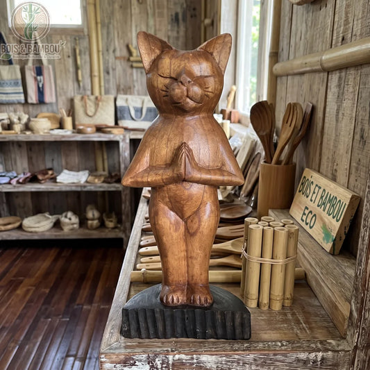 Chat en bois sculpté marron, posture yoga debout mains jointes, posé en boutique artisanale bois et bambou.
