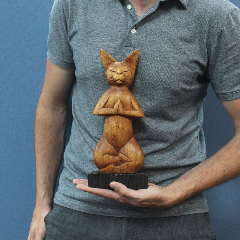Chat en bois sculpté marron, posture yoga lotus, tenu en main pour montrer sa taille compacte.