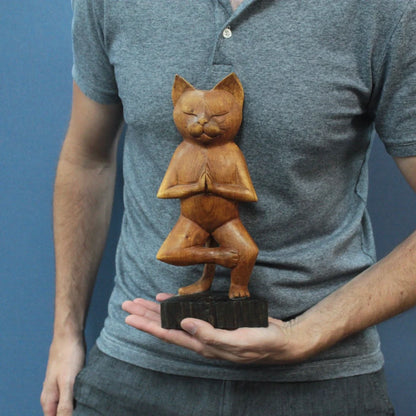 Chat en bois sculpté marron, posture yoga une patte, tenu en main pour montrer sa taille compacte.