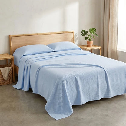 Couverture rafraîchissante en coton bambou, coloris bleu clair, posée sur un lit en bambou tressé