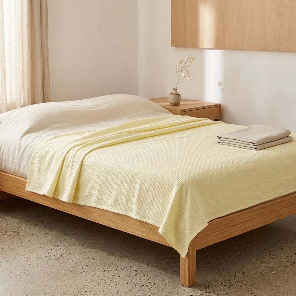 Couverture rafraîchissante en coton bambou, coloris jaune pâle, pliée sur un lit en bois clair
