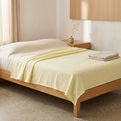 Couverture rafraîchissante en coton bambou, coloris jaune pâle, pliée sur un lit en bois clair