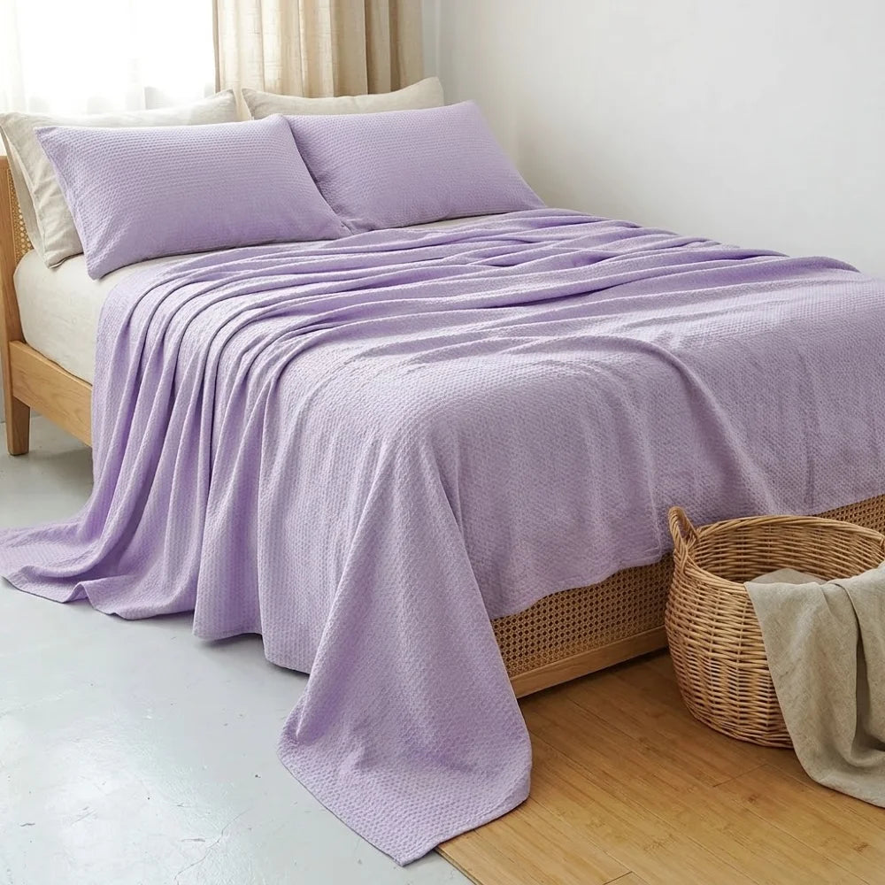 Couverture rafraîchissante en coton bambou, coloris mauve, drapée sur un lit avec taies assorties