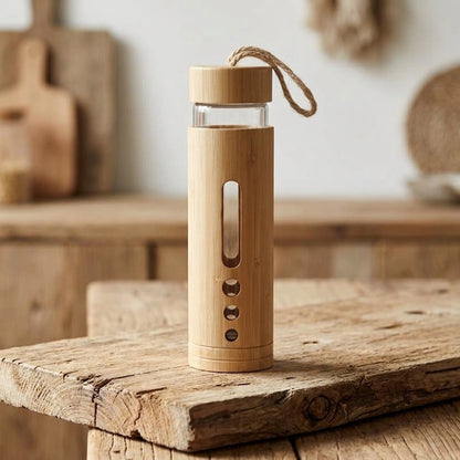 Gourde en bambou et verre borosilicate, grand bouchon, coque en bambou naturel et cordon de transport, posée sur bois brut dans une cuisine