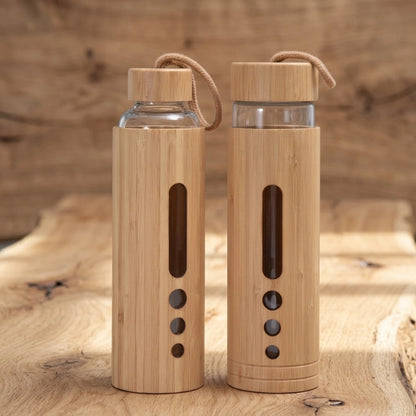 Gourde en bambou et verre borosilicate, coque en bambou naturel avec cordon de transport, deux bouteilles posées sur bois brut