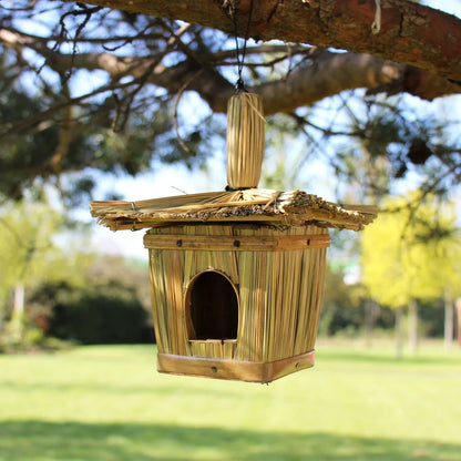 Nichoir à oiseaux en jonc tressé carré, toit en chaume, suspendu à une branche dans un jardin
