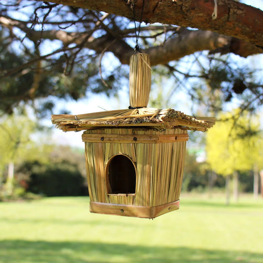 Nichoir à oiseaux en jonc tressé carré, toit en chaume, suspendu à une branche dans un jardin