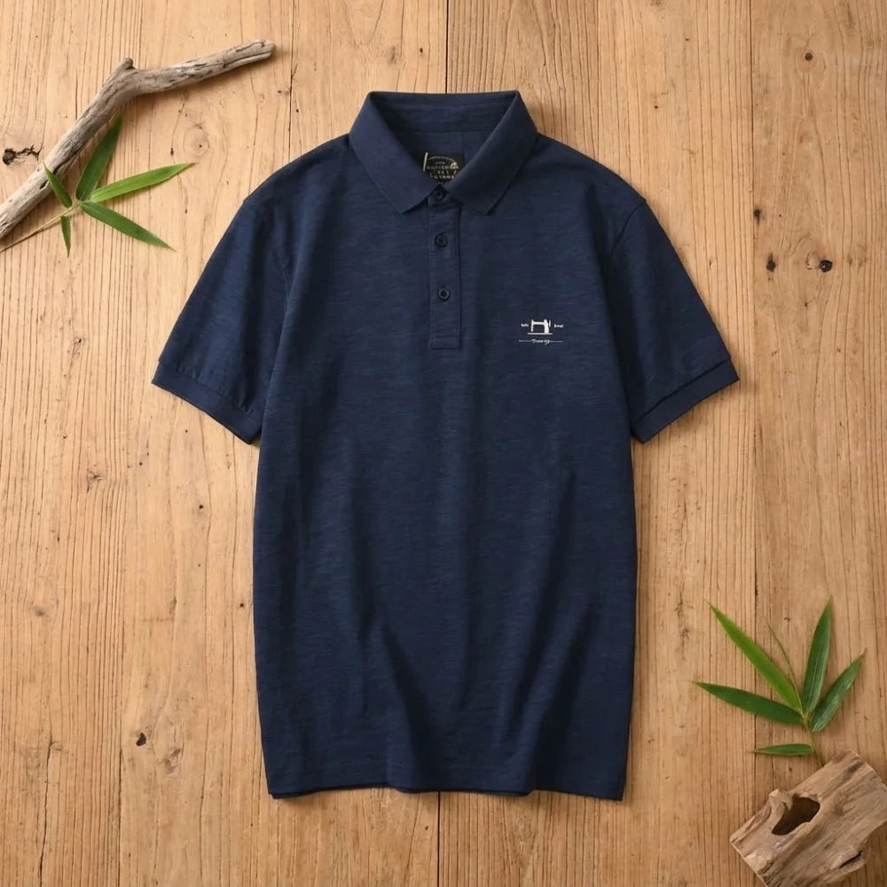 Polo homme bleu marine en coton et fibre de bambou posé à plat sur une table en bois brut avec feuilles de bambou