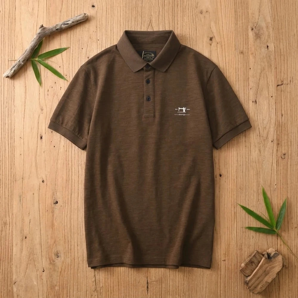 Polo homme café en coton et fibre de bambou posé à plat sur une table en bois brut avec feuilles de bambou