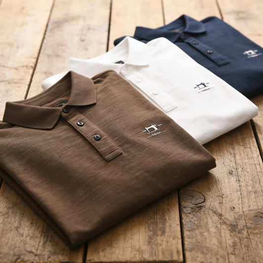 Polos homme en coton et fibre de bambou pliés sur une table en bois, trois coloris café blanc et bleu marine
