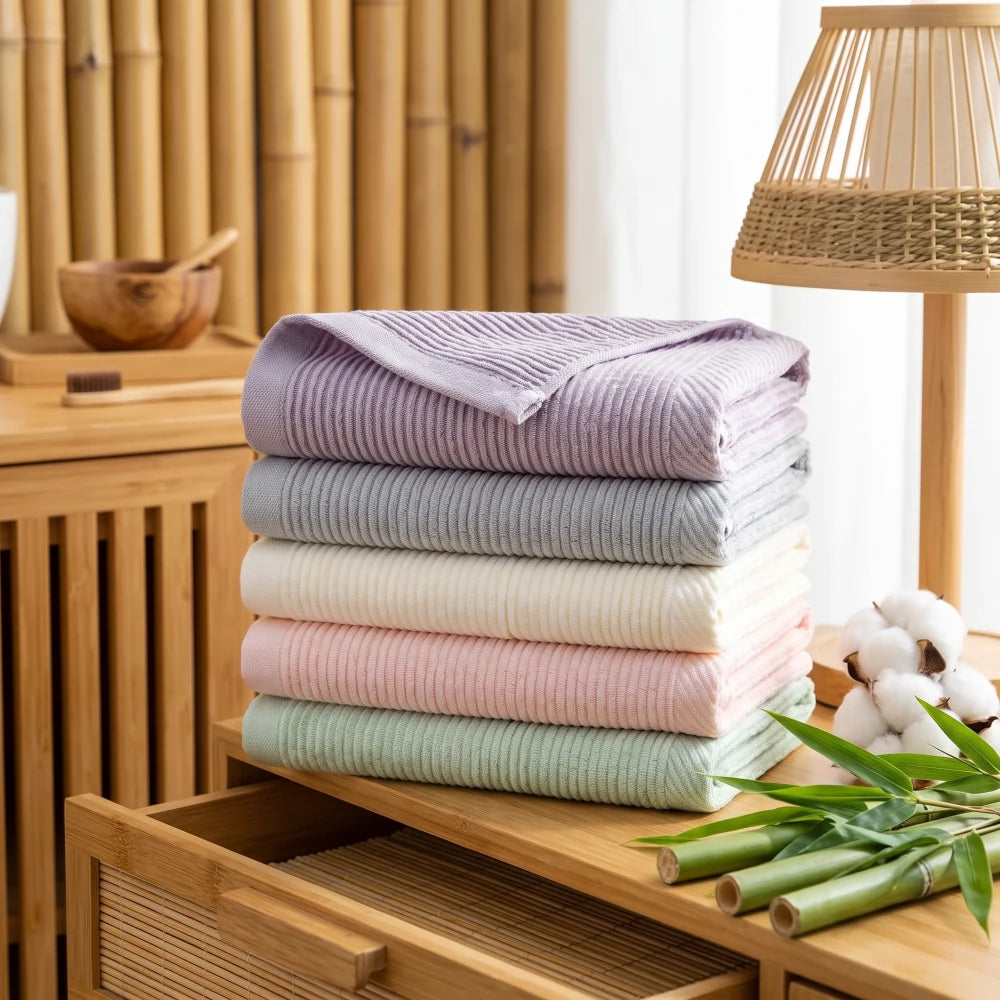 Pile de serviettes en bambou et coton unies, plusieurs coloris, dans une salle de bain en bois et bambou