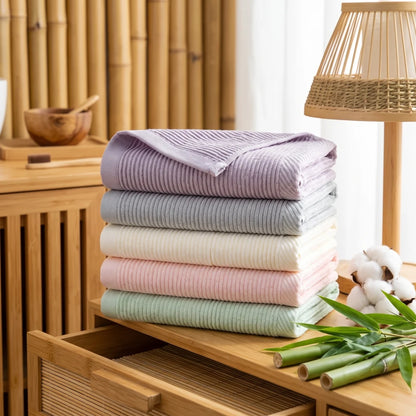 Pile de serviettes en bambou et coton unies, plusieurs coloris, dans une salle de bain en bois et bambou