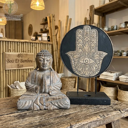 Statue de Bouddha et symbole Hamsa en bois d'albasia gris, posés sur une table en bois dans une boutique de décoration zen