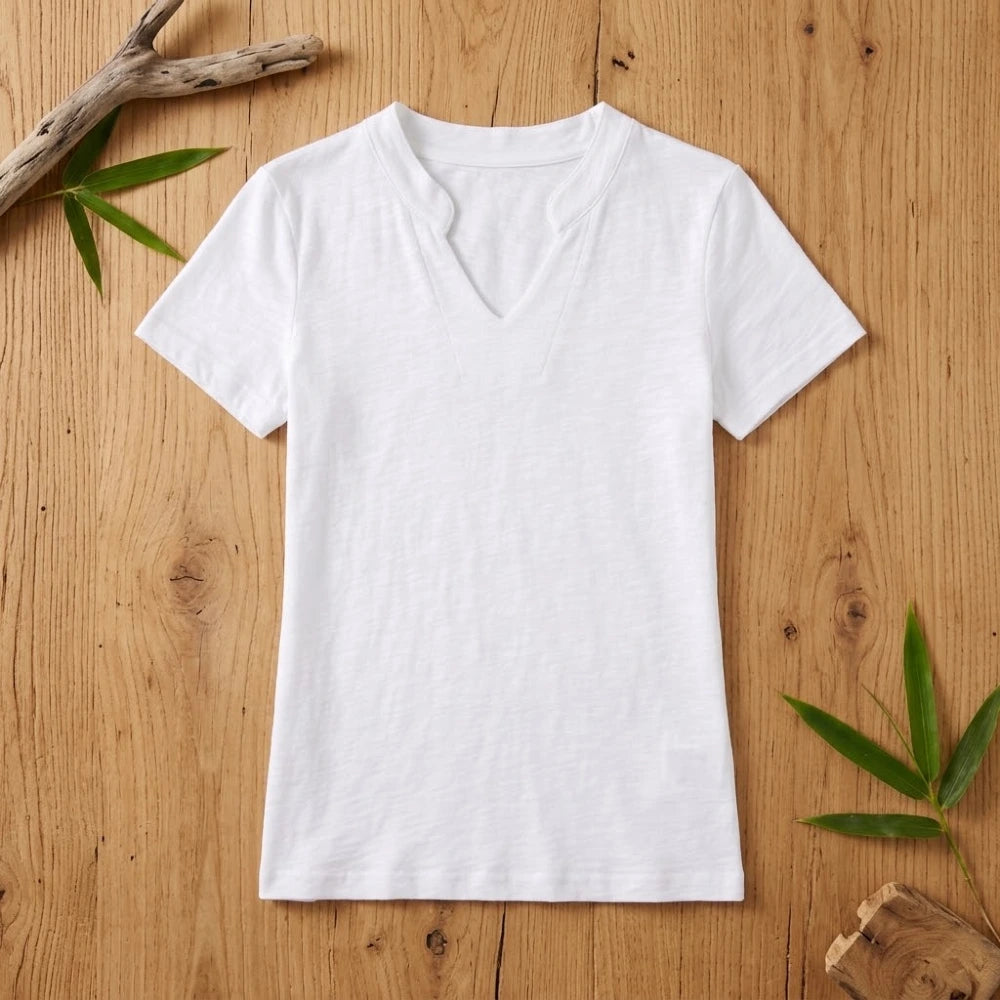 T-shirt femme col V blanc en coton et fibre de bambou posé à plat sur une table en bois brut avec feuilles de bambou