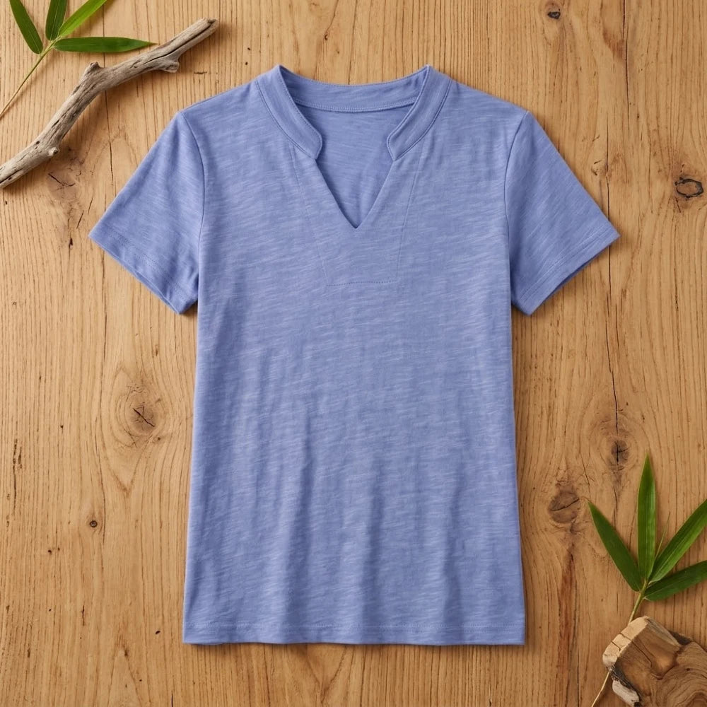 T-shirt femme col V bleu en coton et fibre de bambou posé à plat sur une table en bois brut avec feuilles de bambou