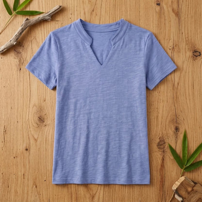 T-shirt femme col V bleu en coton et fibre de bambou posé à plat sur une table en bois brut avec feuilles de bambou