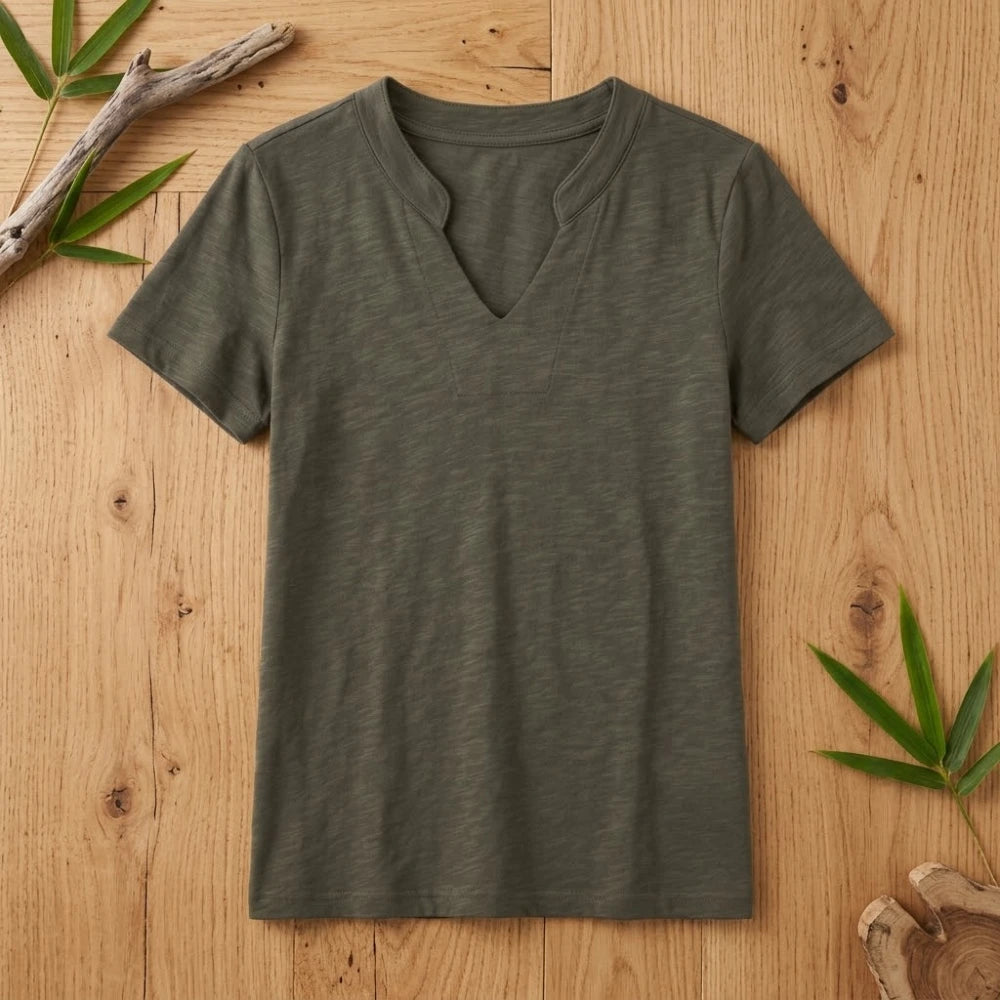 T-shirt femme col V vert kaki en coton et fibre de bambou posé à plat sur une table en bois brut avec feuilles de bambou