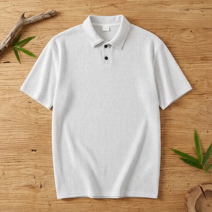 Polo homme en maille de bambou blanc posé à plat sur une table en bois brut avec feuilles de bambou