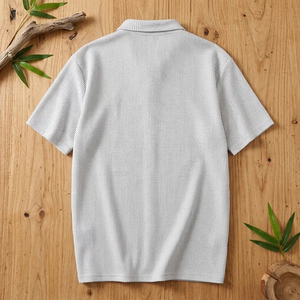 Polo homme en maille de bambou vu de dos, posé à plat sur une table en bois brut avec feuilles de bambou