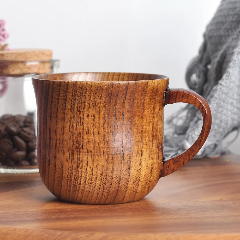 Tasse en bois naturel posée sur une table, entourée de grains de café et d'un plaid en laine grise.