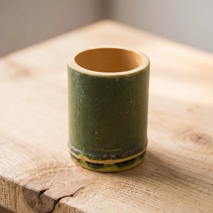 Tasse en bambou naturel ronde posée sur une table en bois clair, bambou vert avec base foncée
