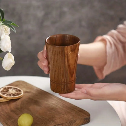 Tasse en bois tenue à deux mains au-dessus d'une planche en bois avec tranches d'orange séchées