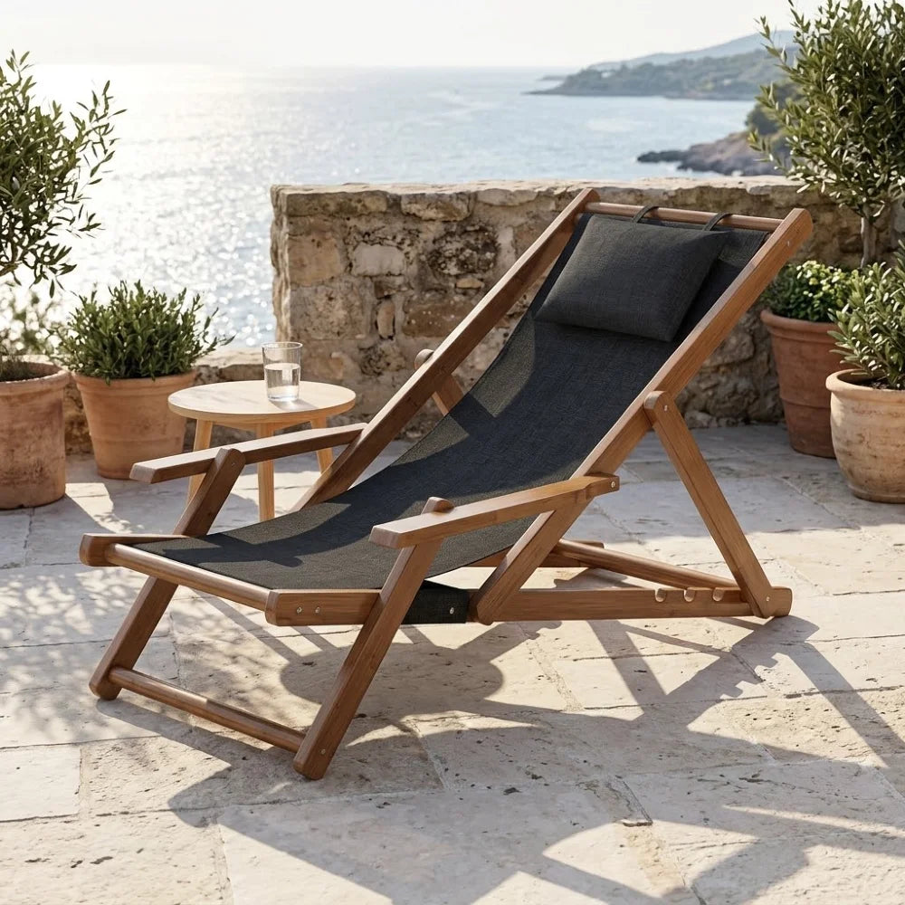 Transat en toile et bambou à accoudoirs, cadre brun et toile noire avec coussin assorti, sur une terrasse en pierre