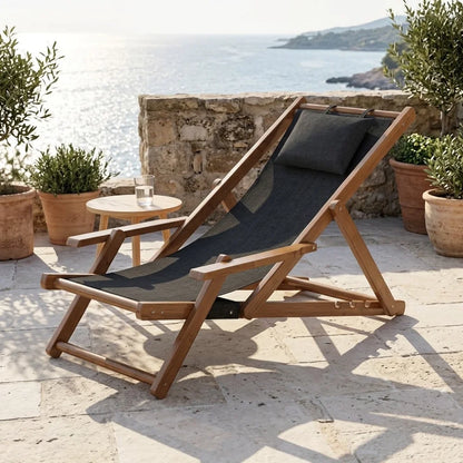 Transat en toile et bambou à accoudoirs, cadre brun et toile noire avec coussin assorti, sur une terrasse en pierre