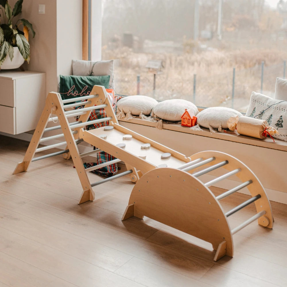 Triangle Montessori XXL en bois avec arche Pikler et mur d'escalade à prises, installé devant une baie vitrée