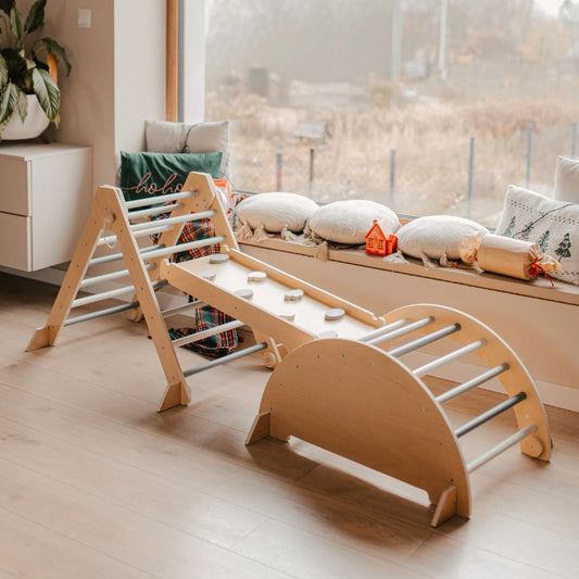 Triangle Montessori XXL en bois avec arche Pikler et mur d'escalade à prises, installé devant une baie vitrée